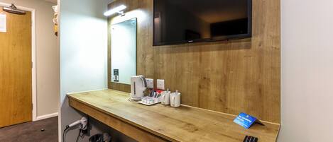 Une chambre d’hôtel équipée d’un bureau en bois, d’un téléviseur à écran plat fixé au mur, d’un sèche-cheveux, d’une bouilloire et d’une télécommande.