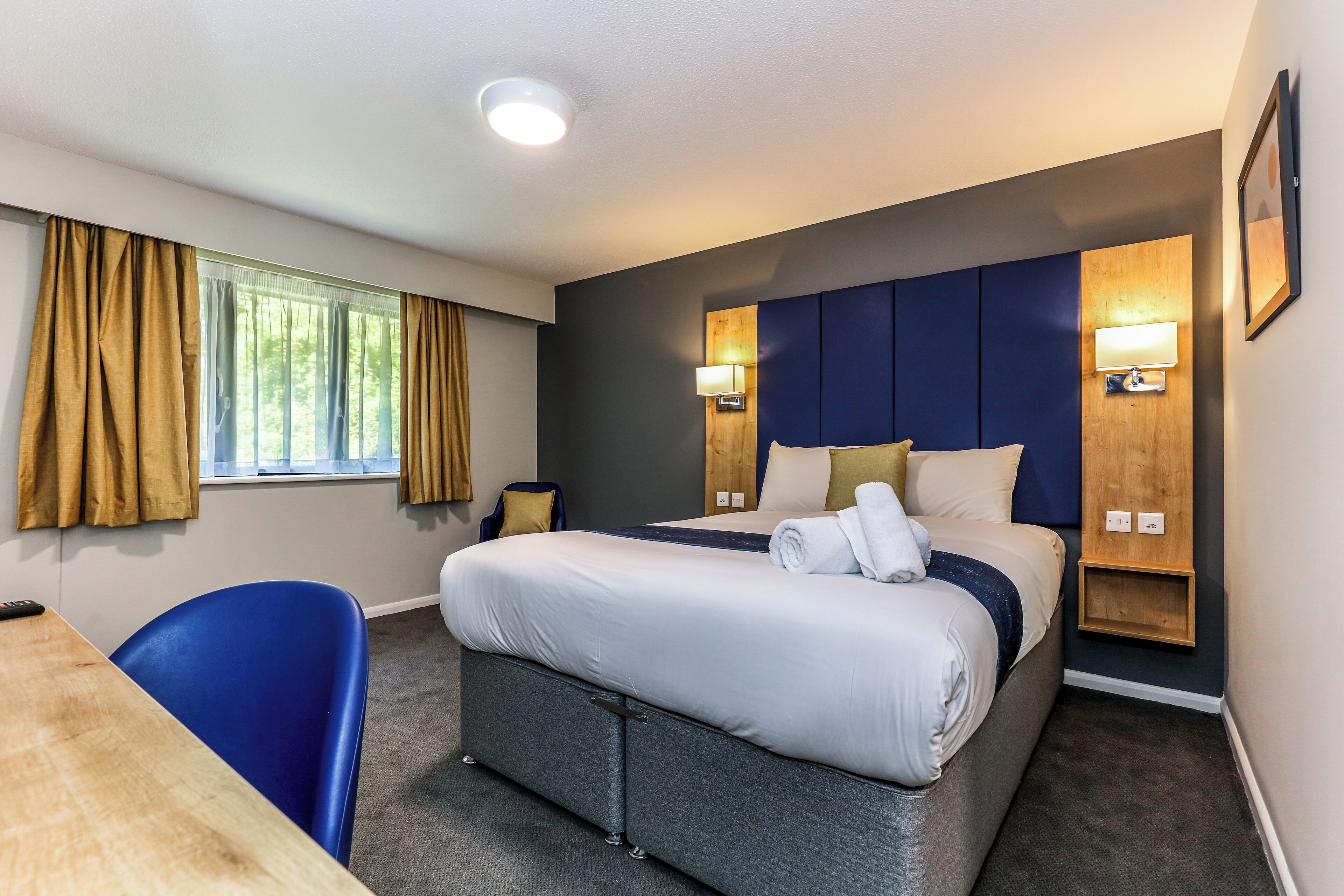 Een hotelkamer met een bed, nachtkastjes, een bureau en een stoel.