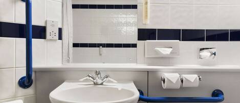 Un baño con un lavamanos blanco, barras de apoyo azules, un espejo y un perchero para toallas.