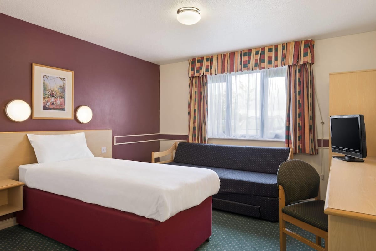 A hotel room with a bed, a desk, a chair, a sofa, a television, and a window with curtains.