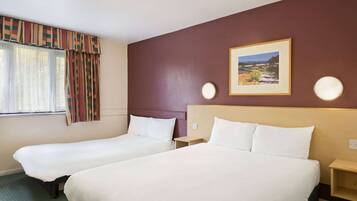 A hotel room with two single beds, a large window with curtains, a framed picture on the wall, and bedside lamps.