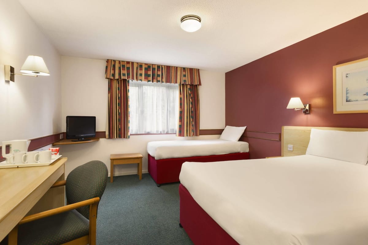A hotel room with a bed, a desk with a computer, a chair, a television, and a window with curtains.