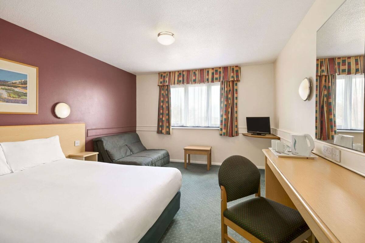 A hotel room with a bed, a desk, a chair, a television, and a window with curtains.