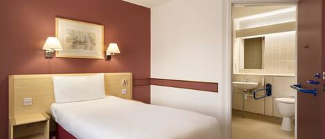 A hotel room with a bed, bedside tables, a wall-mounted lamp, a framed picture, and a bathroom with a sink and toilet.