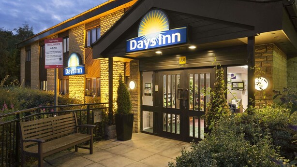 Un hôtel Days Inn doté d’une entrée bien éclairée, d’un banc à l’extérieur et d’un panneau indiquant que le stationnement est gratuit pour les clients de l’hôtel.