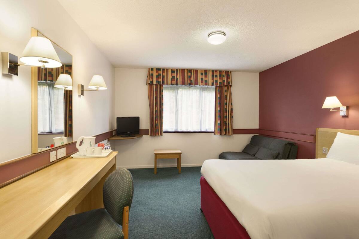 Une chambre d’hôtel comprenant un lit, un bureau avec une chaise, une télévision et une petite table.