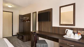 A hotel room with a bed, a desk with a tray of breakfast items, a TV, a mirror, and a coat rack.