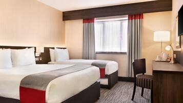 A hotel room with two beds, a desk, a chair, a lamp, and a window with curtains.