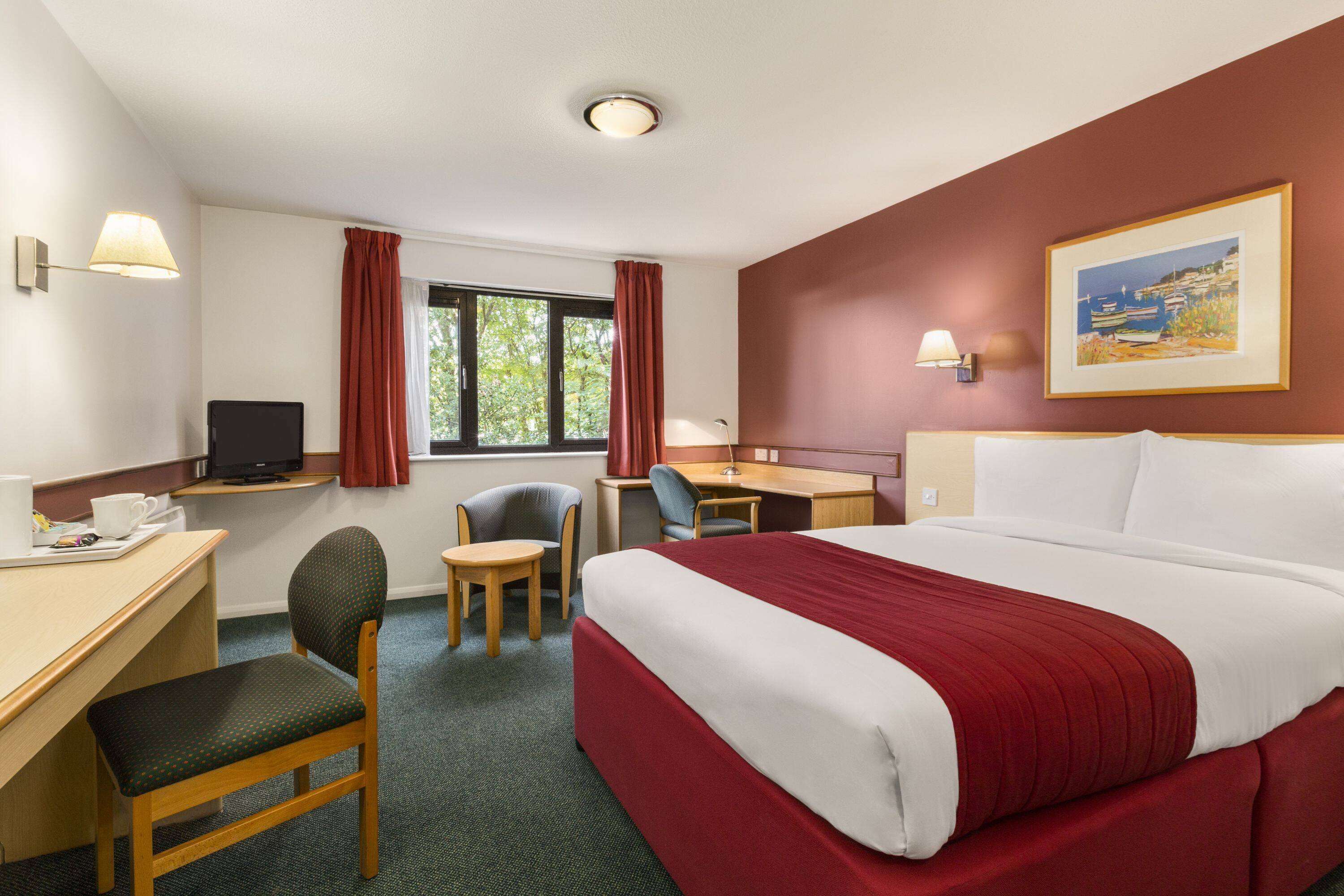 A hotel room with a bed, desk, chair, television, and a window with curtains.