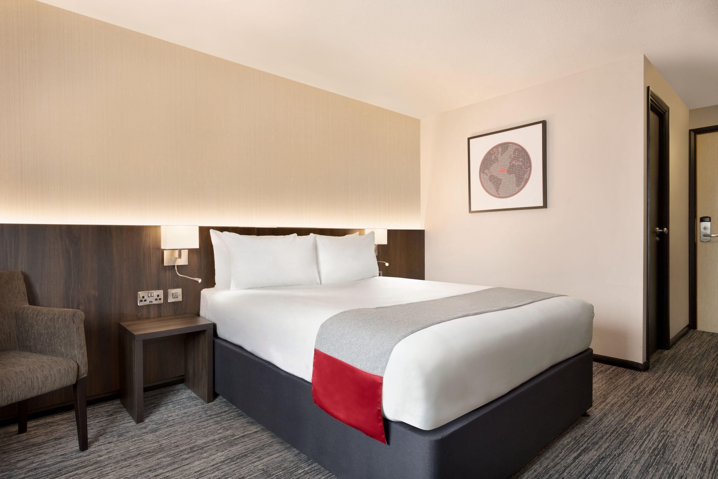 A hotel room with a bed, a nightstand, a chair, and a door.