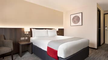 A hotel room with a bed, a nightstand, a chair, and a door.