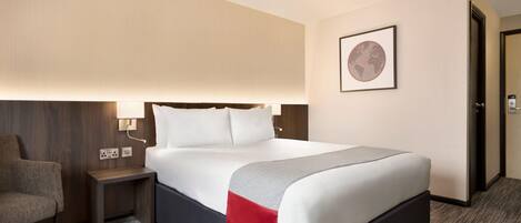 A hotel room with a bed, a nightstand, a chair, and a door.