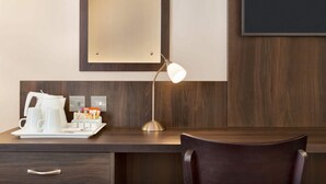Une chambre d’hôtel avec un bureau en bois, une machine à café blanche, une lampe et un miroir.