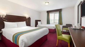 Hotelkamer met een groot bed, een kleiner bed, een bureau met stoel en een raam met gordijnen.