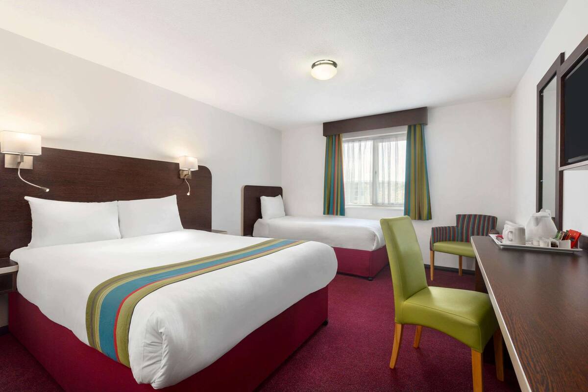 Hotelkamer met een groot bed, een kleiner bed, een bureau met stoel en een raam met gordijnen.