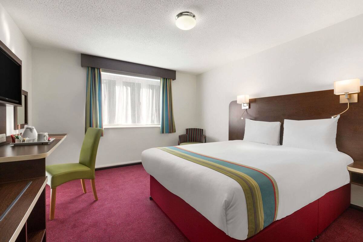 Een hotelkamer met een groot bed, een bureau met stoel, een televisie en een raam met gordijnen.