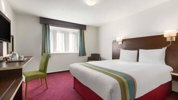 A hotel room with a large bed, a desk with a chair, a television, and a window with curtains.
