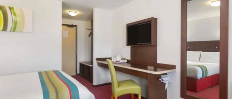 Habitación de hotel con cama, escritorio, silla, televisor y un espejo grande.