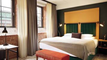 Ein Hotelzimmer mit einem großen Bett, einer Bank, einem Schreibtisch und einem Fenster mit Vorhängen.
