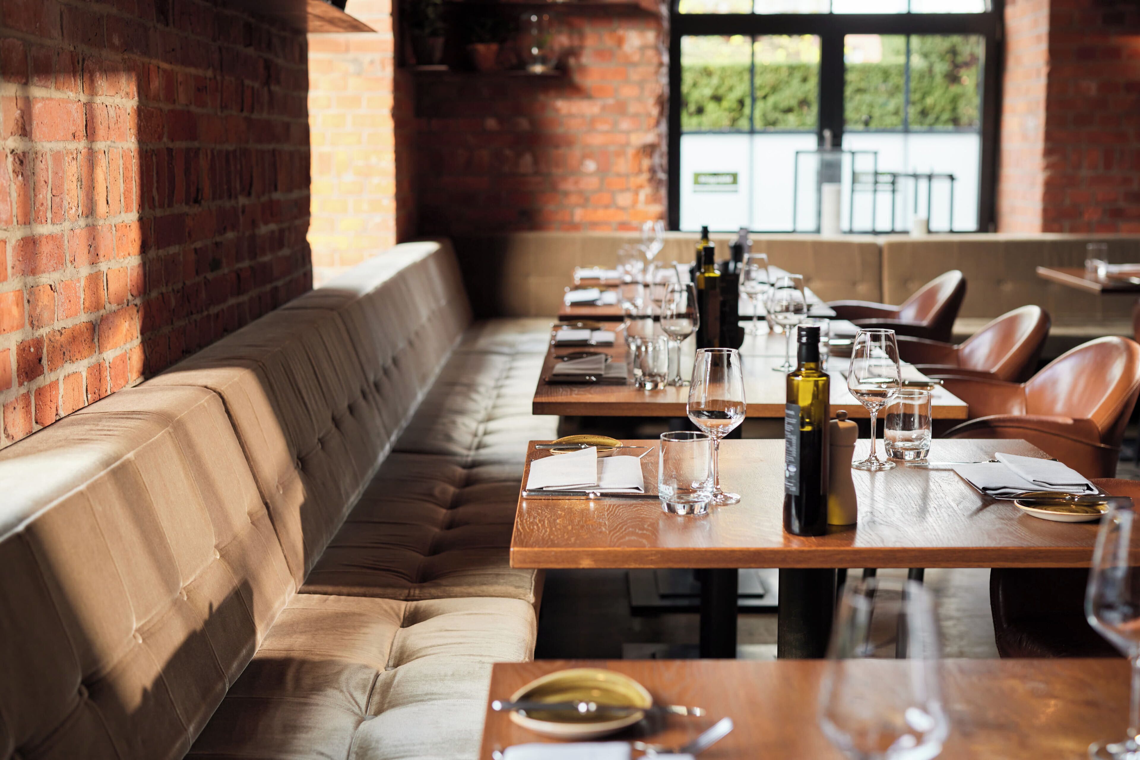 Un restaurante con una larga mesa de madera dispuesta para comer, un banco acolchado a lo largo de la pared y un muro de ladrillo.