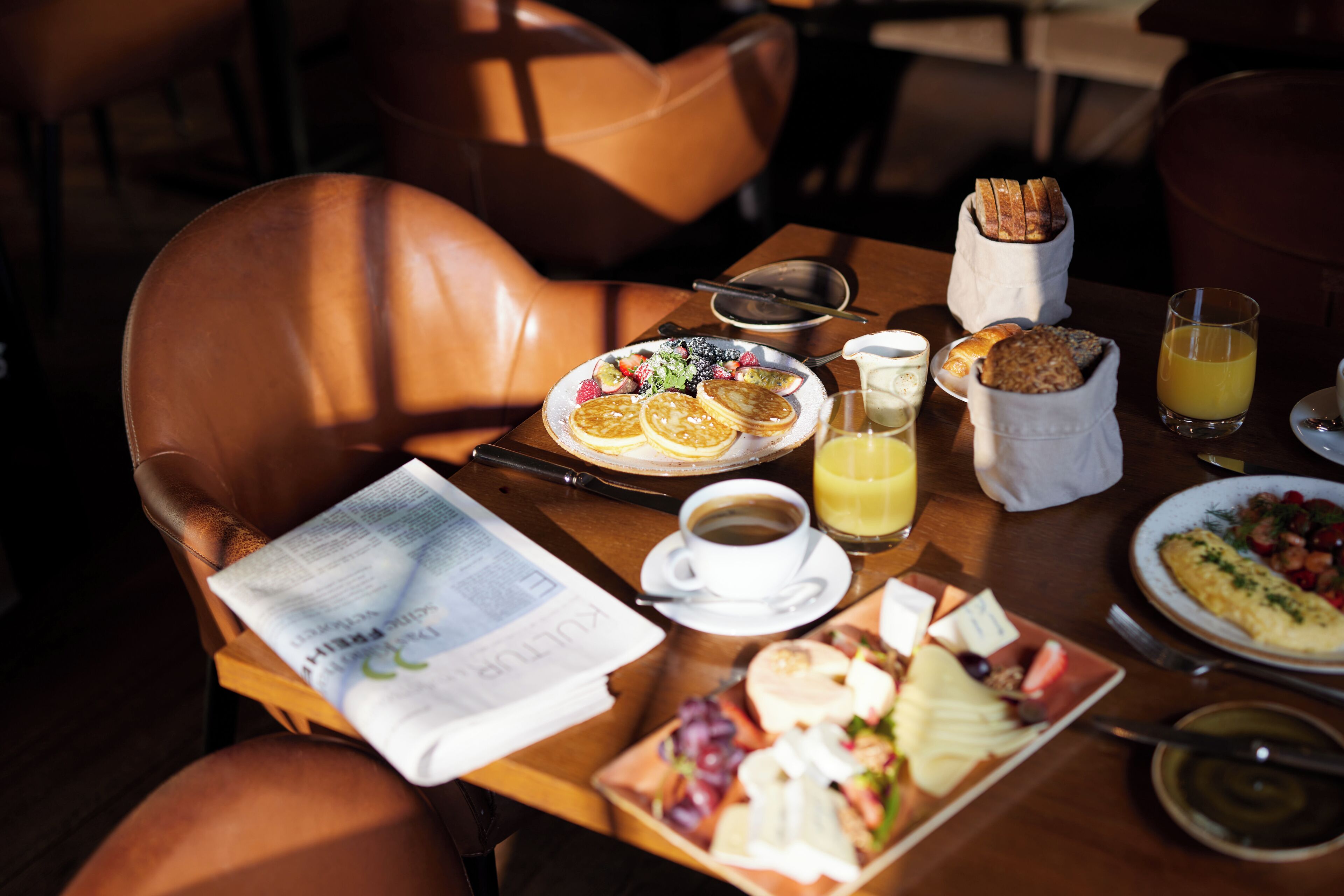 Una tavola imbandita per la colazione, con diversi cibi, un giornale e una tazza di caffè.