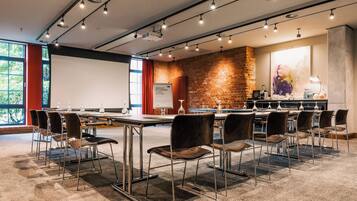 Une salle de conférence avec une longue table, des chaises, un écran de projection et un mur en briques.