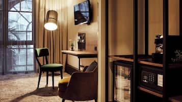 A hotel room with a large window, a desk with a chair, a television, and a coffee machine.