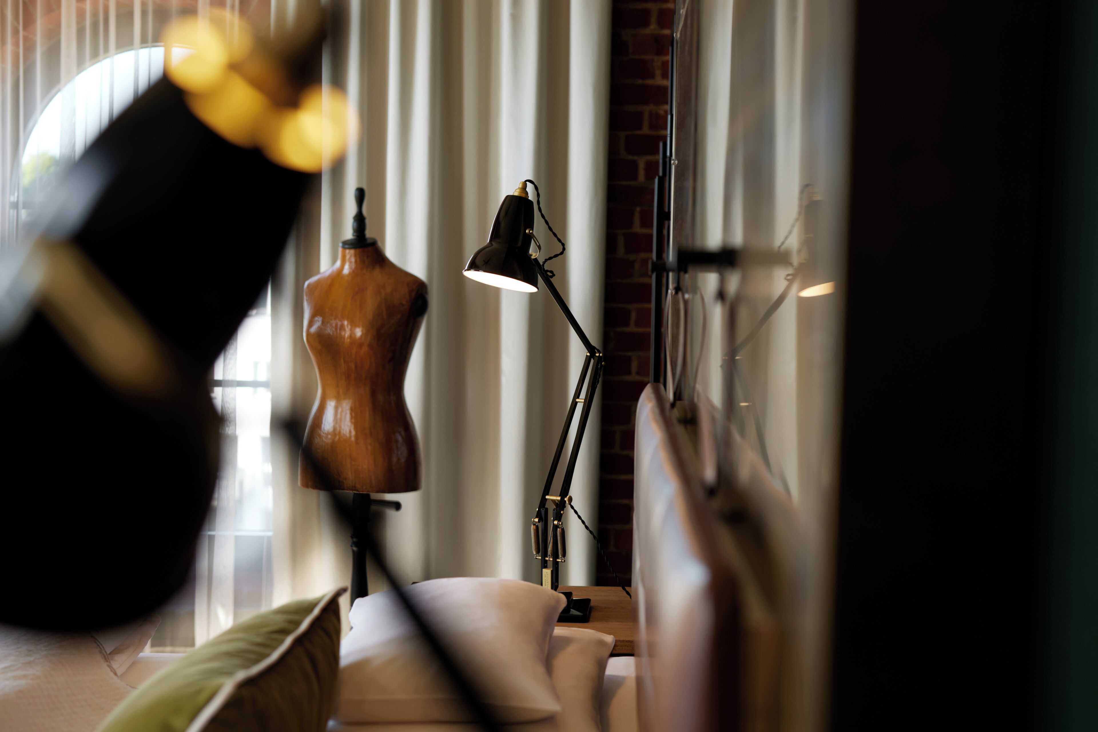 Une pièce comprenant un mannequin, une lampe de bureau et une fenêtre avec des stores.