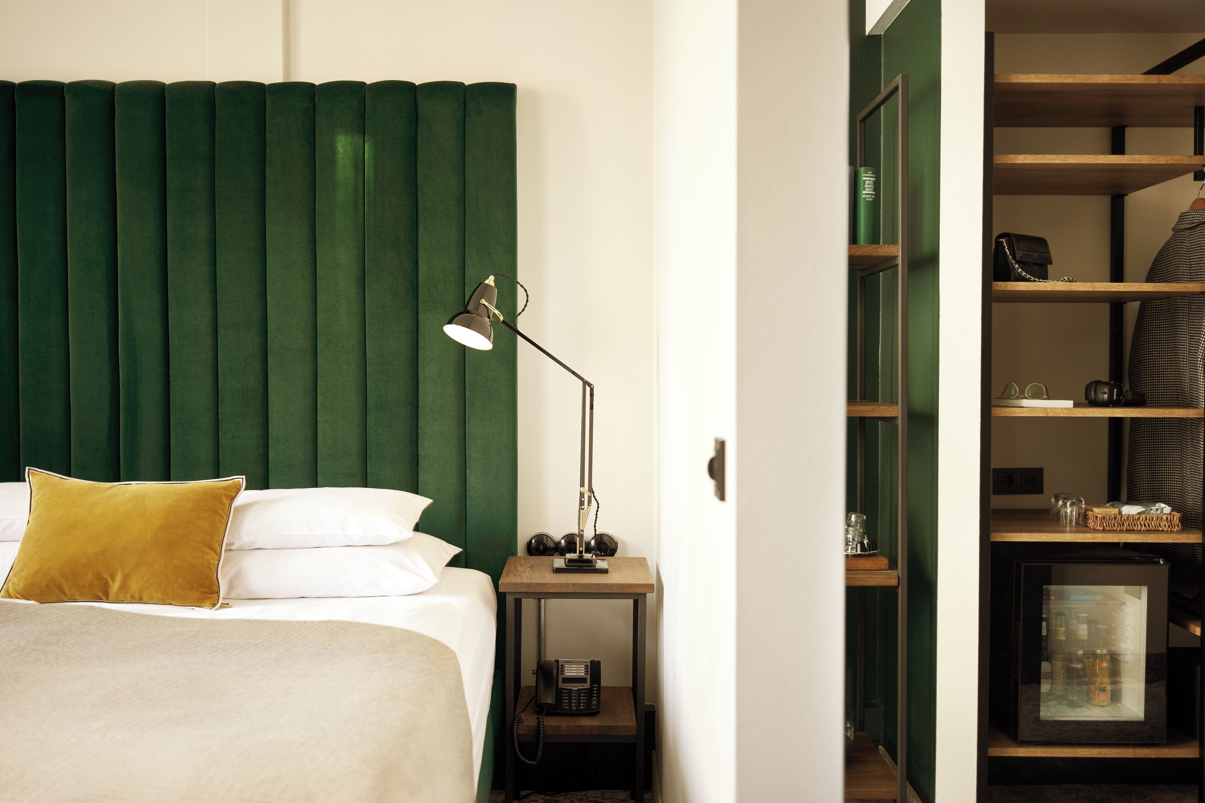 Una cama bien hecha con un cabecero verde, una lámpara de noche y una mesita de noche con un teléfono.
