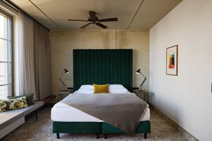 Une chambre à coucher avec un lit, un ventilateur de plafond, une fenêtre avec des rideaux et un tableau accroché au mur.