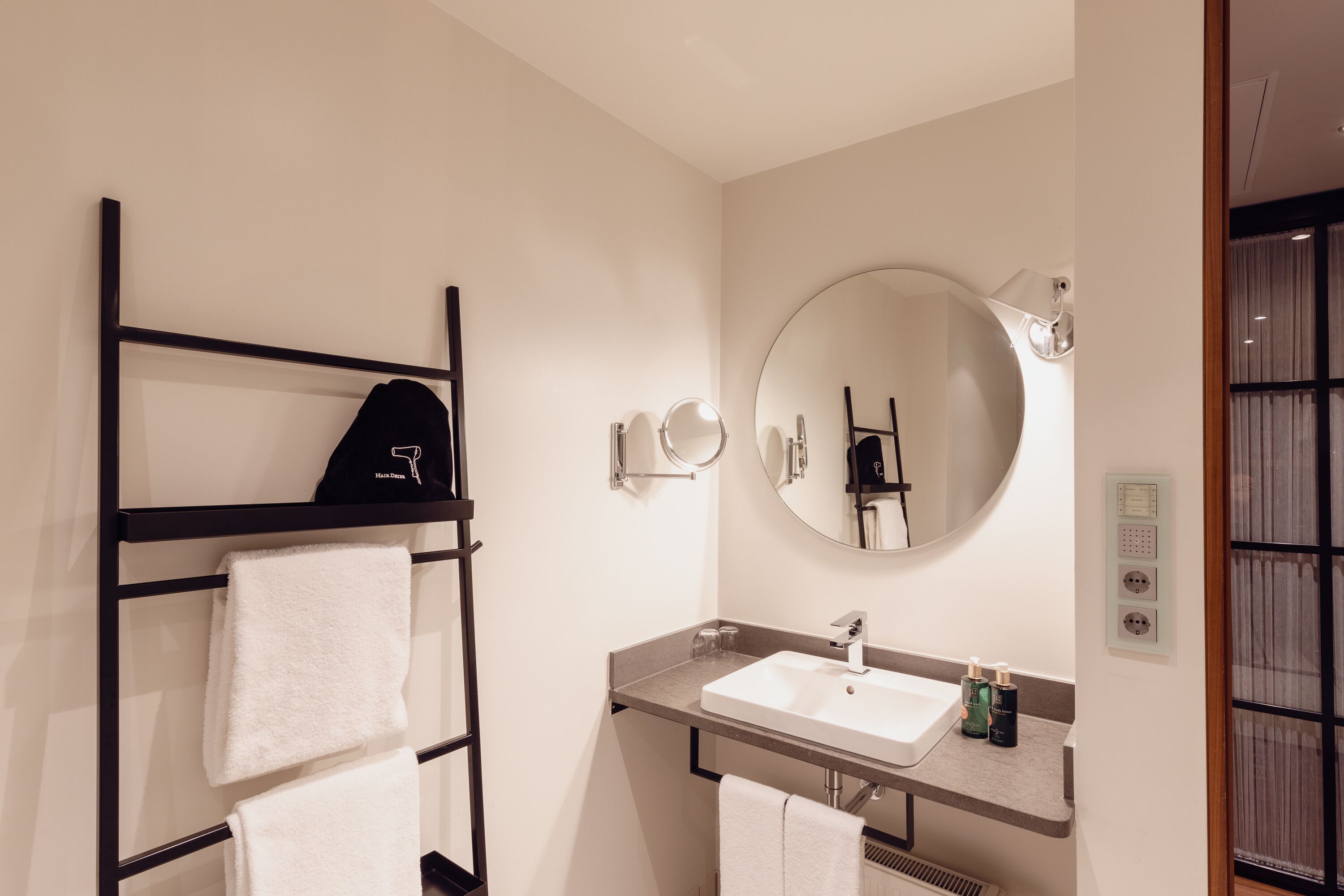 A modern bathroom with a black towel rack, a round mirror, a sink, and a towel hanging on the rack.