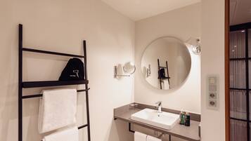 A modern bathroom with a black towel rack, a round mirror, a sink, and a towel hanging on the rack.