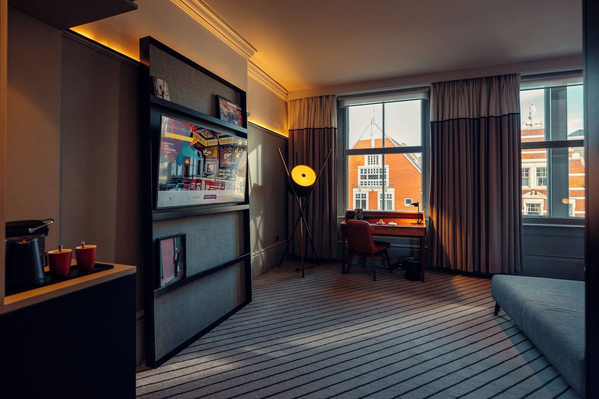 Een hotelkamer met een groot raam, een bureau, een stoel, een boekenkast en een bank.