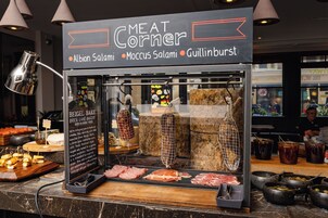 A meat counter with various meats and condiments, including a sign for 'Meat Corner' with names like Albion Salami, Moccus Salami, and Guillinburst.