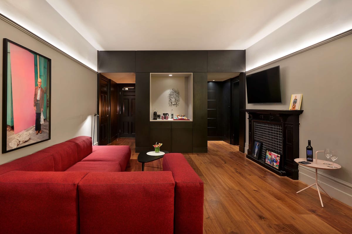 Een moderne woonkamer met een rode bank, een klein rond tafeltje met een vaas, en een open haard.