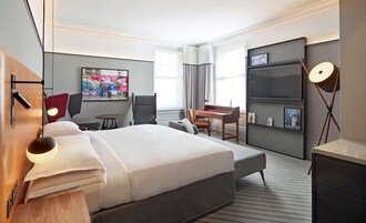 Ein modernes Hotelzimmer mit einem großen Bett, einem Schreibtisch, einem Stuhl und einem kleinen Tisch.