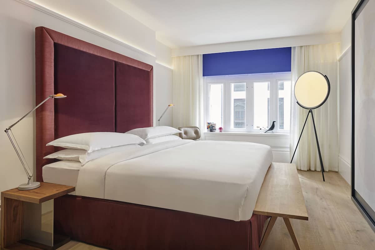 Een moderne hotelkamer met een groot bed, nachtlampjes, een ronde spiegel en uitzicht op de stad door het raam.