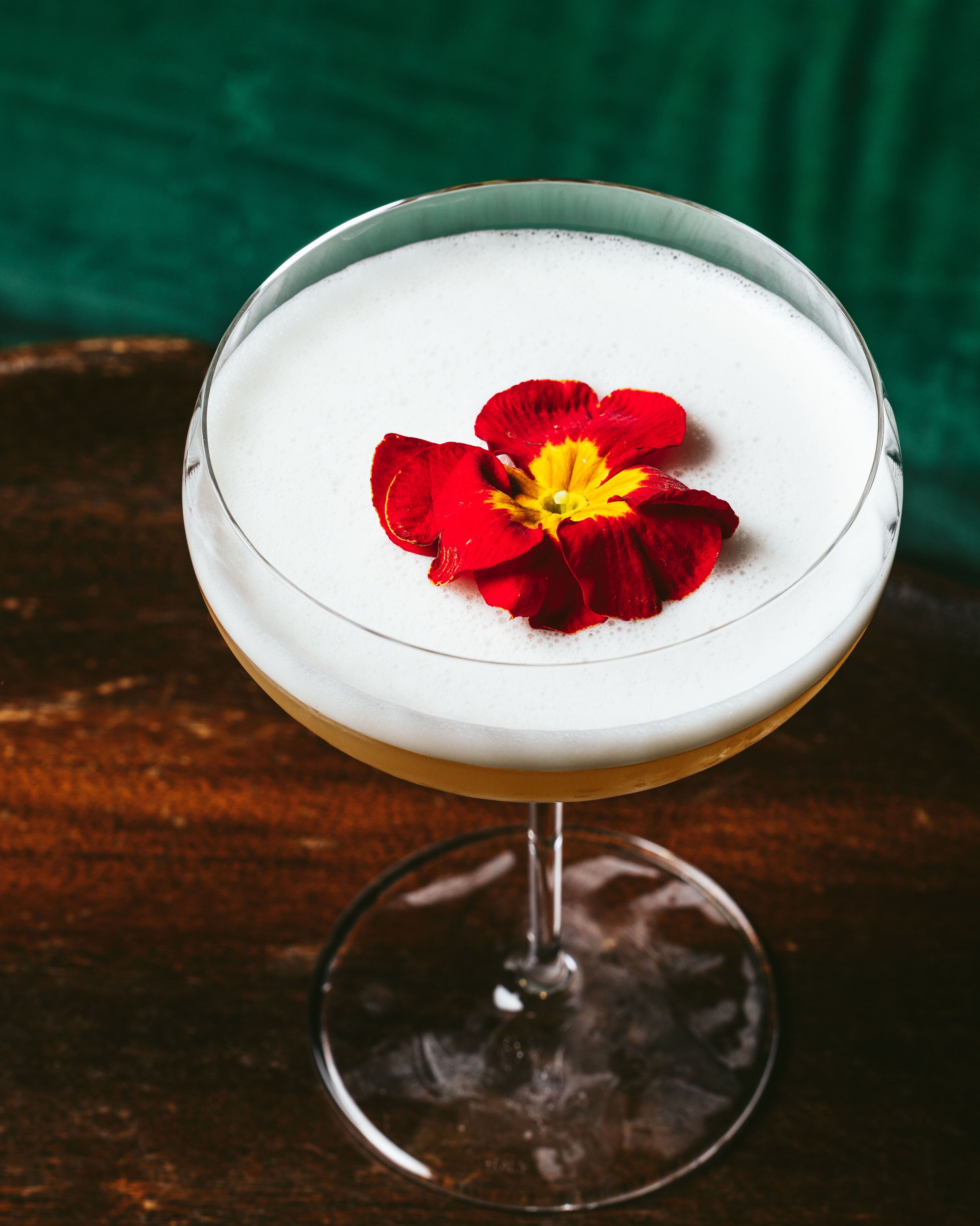 Un cóctel en una copa de martini adornado con una flor roja.