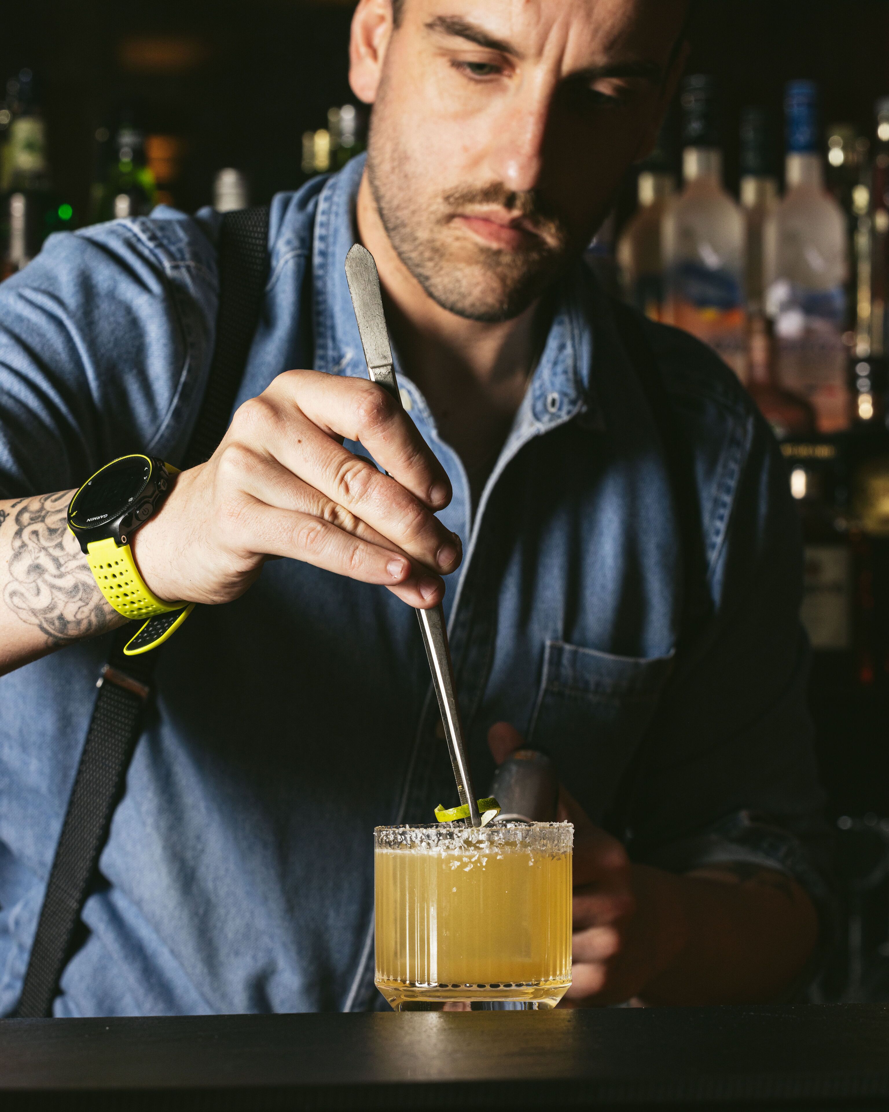 A person holding a drink with a straw, wearing a watch, and a denim shirt.