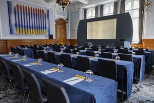 Ein Konferenzraum mit Reihen von Tischen, einer großen Leinwand und einem Projektor.