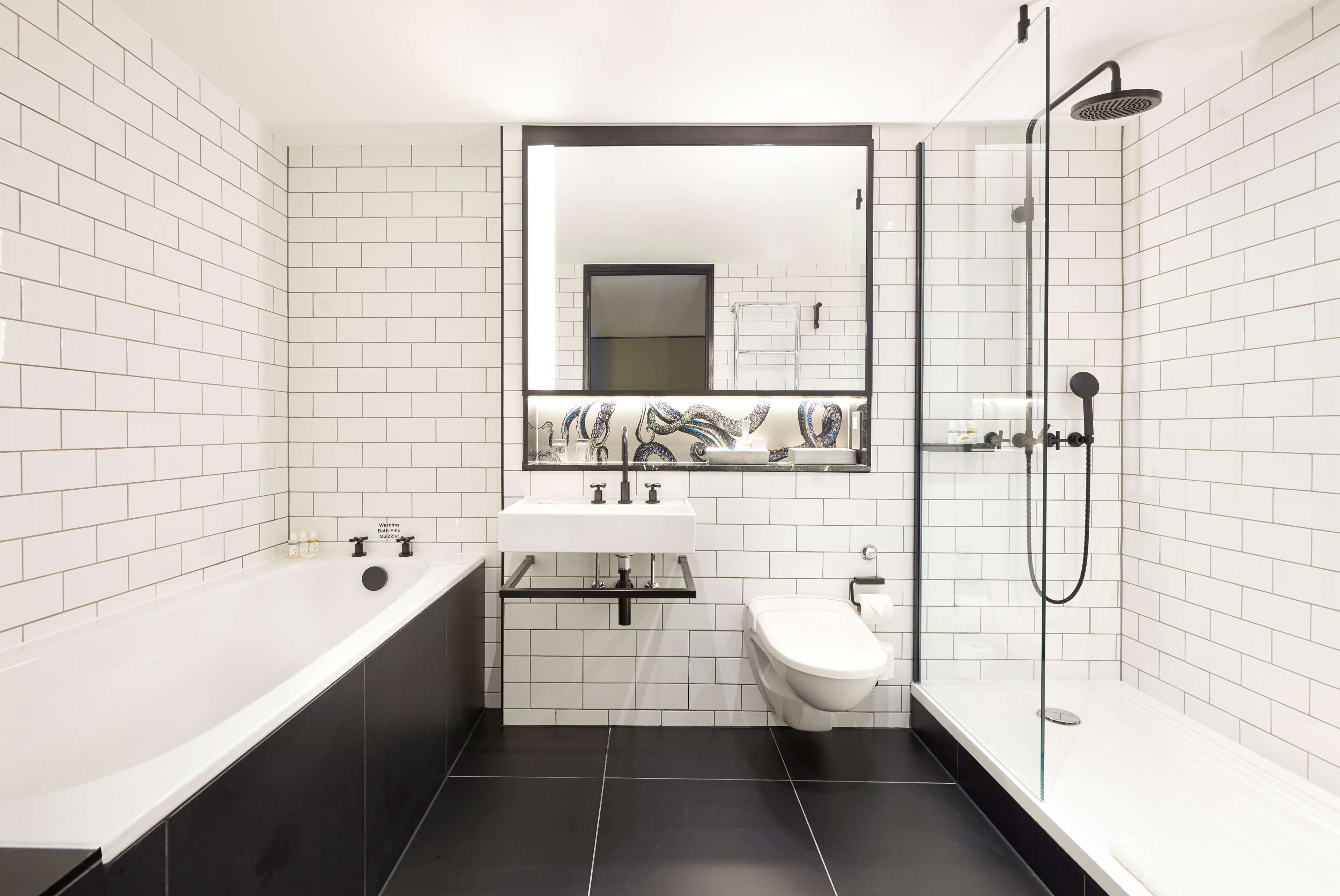 Une salle de bain moderne avec des murs recouverts de carreaux blancs, une baignoire noire, un lavabo blanc et une douche à parois de verre.