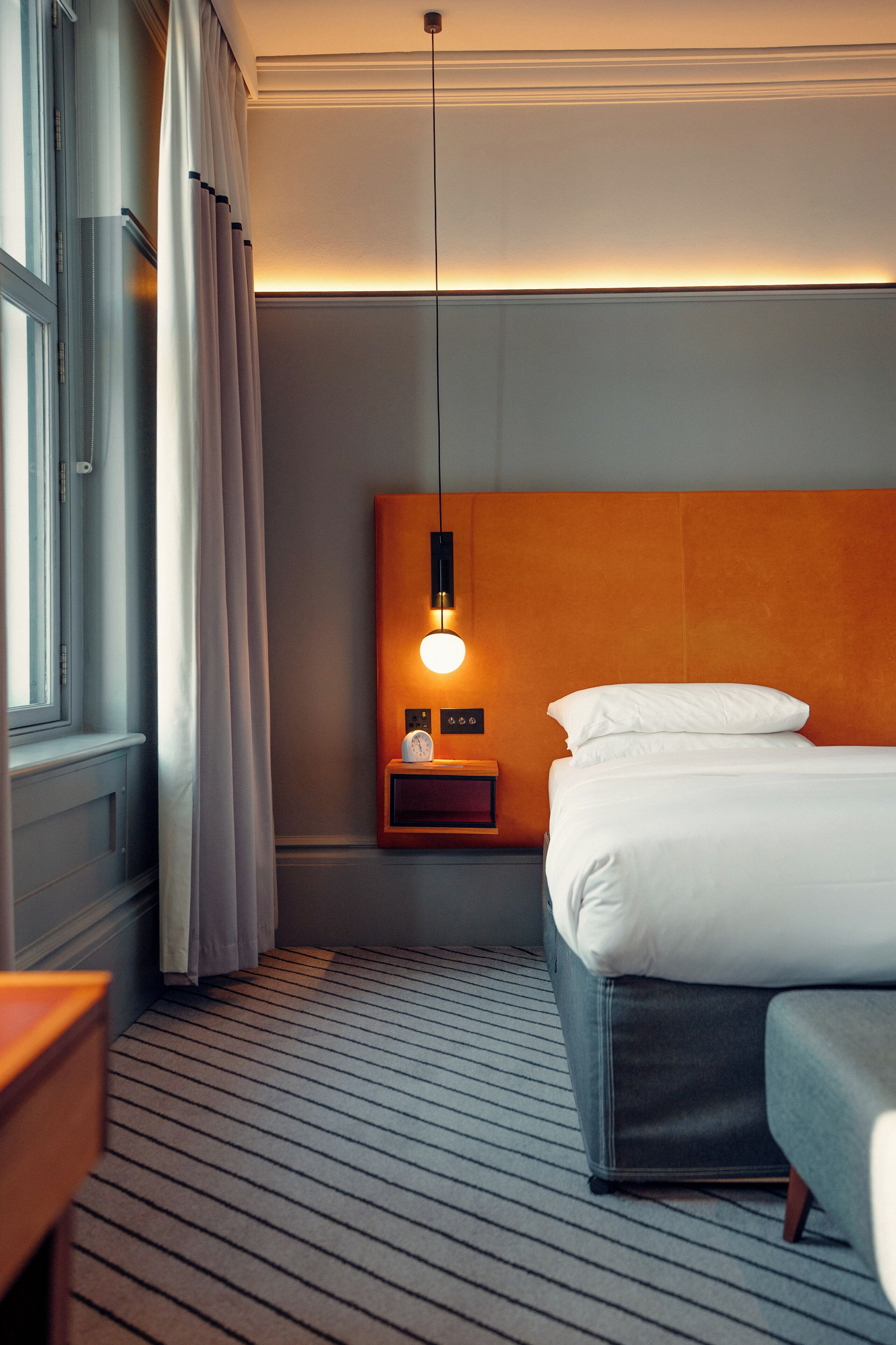 A hotel room with a bed, bedside table, and a wall-mounted light fixture.