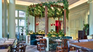 A dining area with wooden tables and chairs, a green cushioned seating area, and a decorative ceiling with greenery. - ANDAZ LONDON LIVERPOOL STREET, BY HYATT (London)