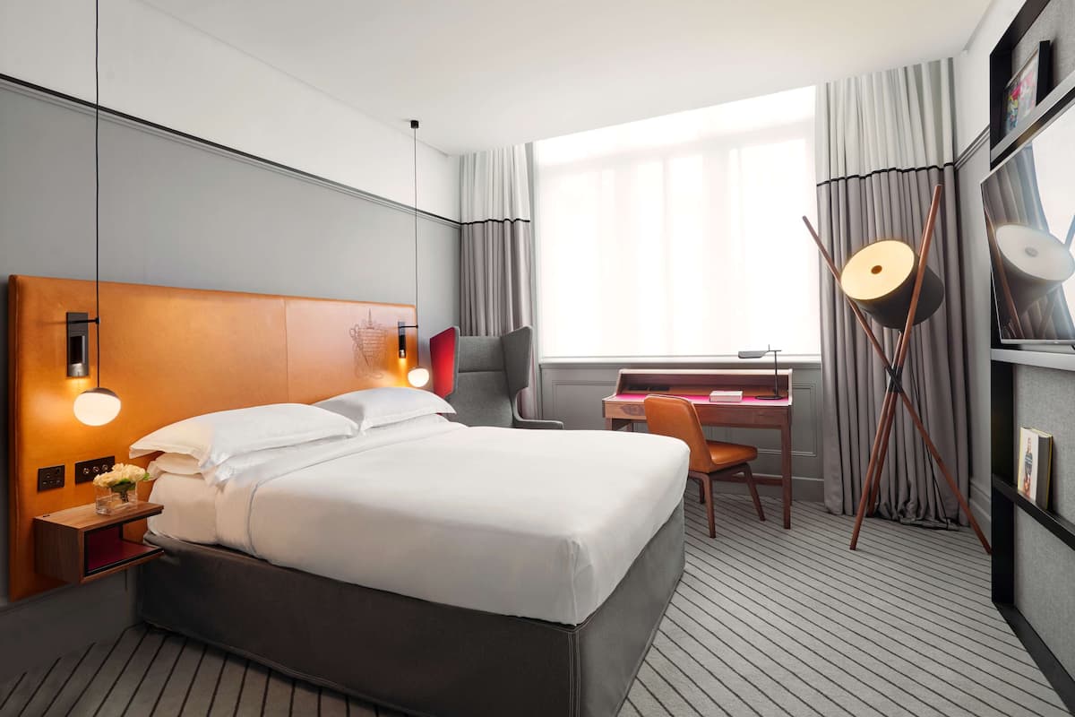 Een hotelkamer met een groot bed, een bureau, een stoel, een lamp en een raam met gordijnen.