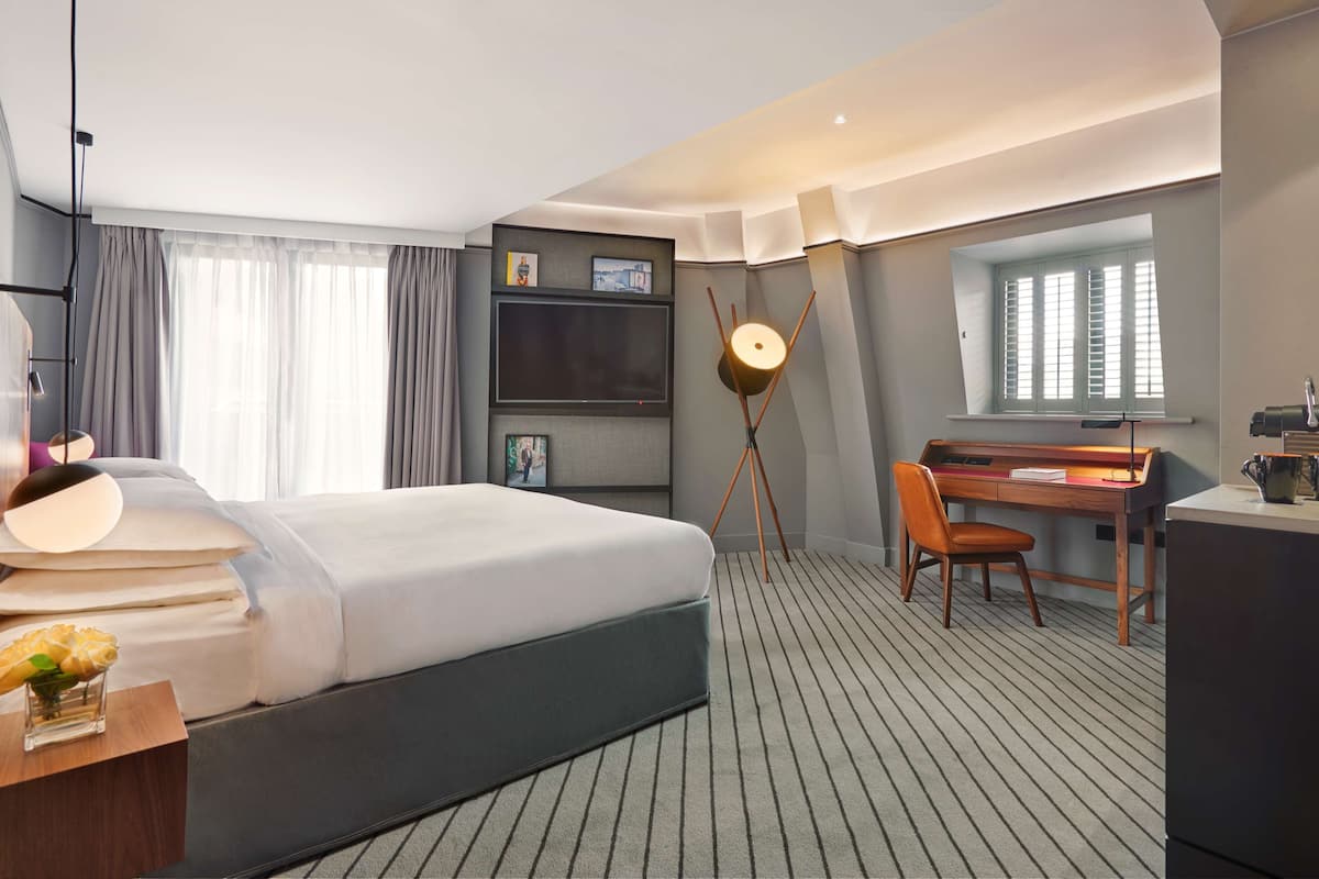 Een hotelkamer met een bed, bureau, stoel en een groot raam.