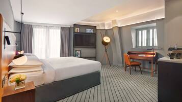 A hotel room with a bed, desk, chair, and a large window.