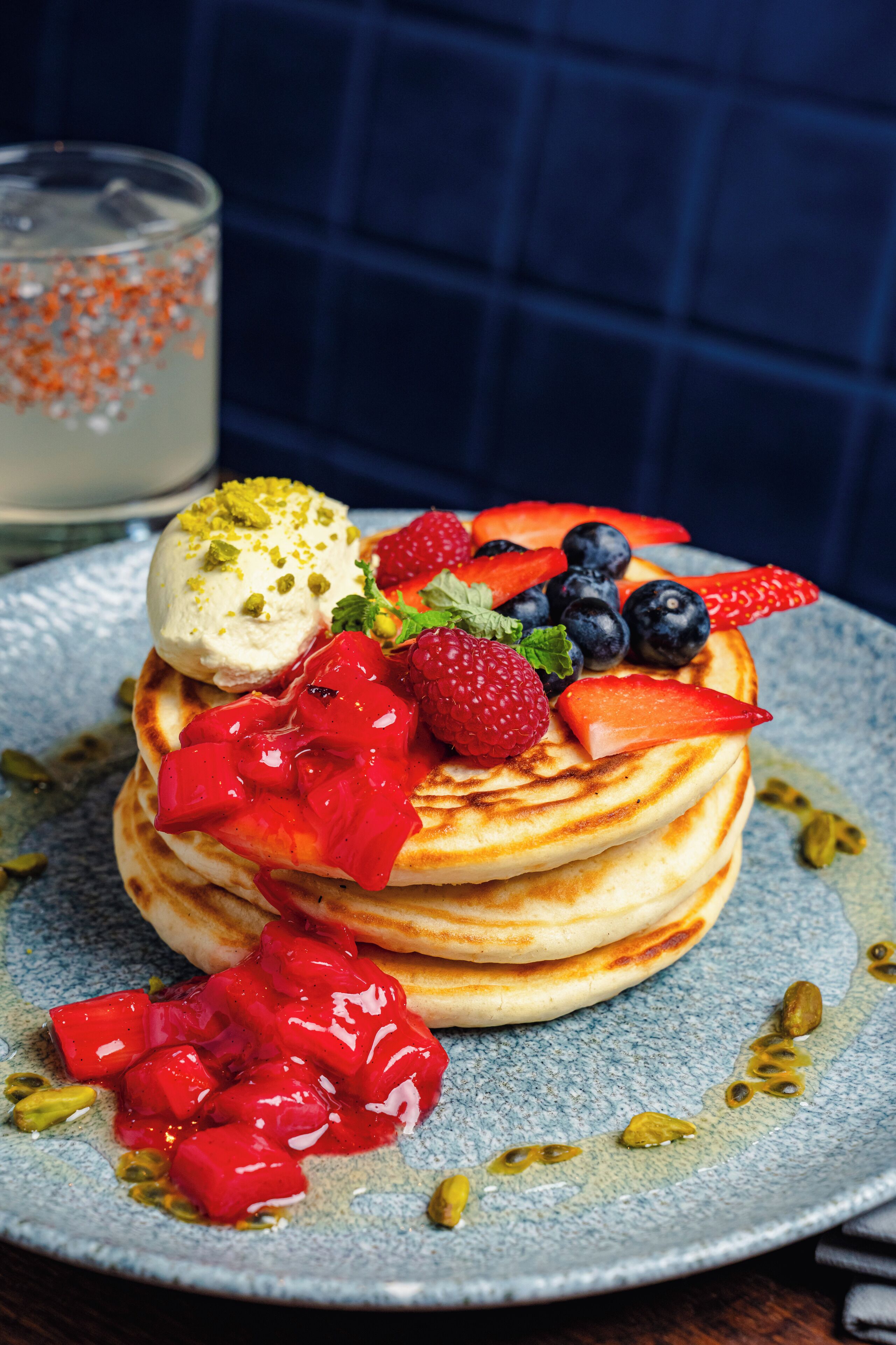 A stack of pancakes with fruit and a scoop of ice cream on a blue plate.