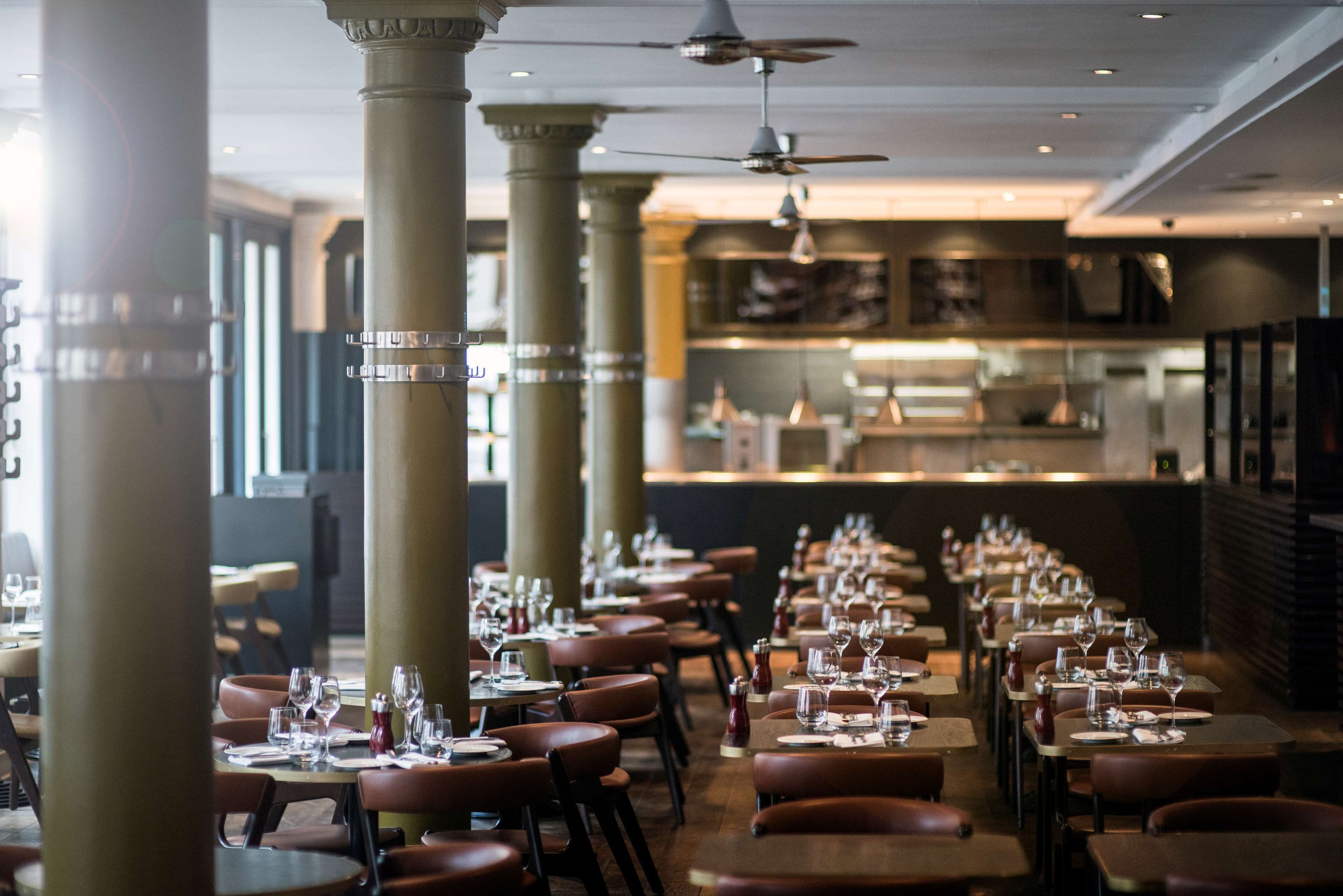 A restaurant with long tables, brown leather chairs, and ceiling fans.