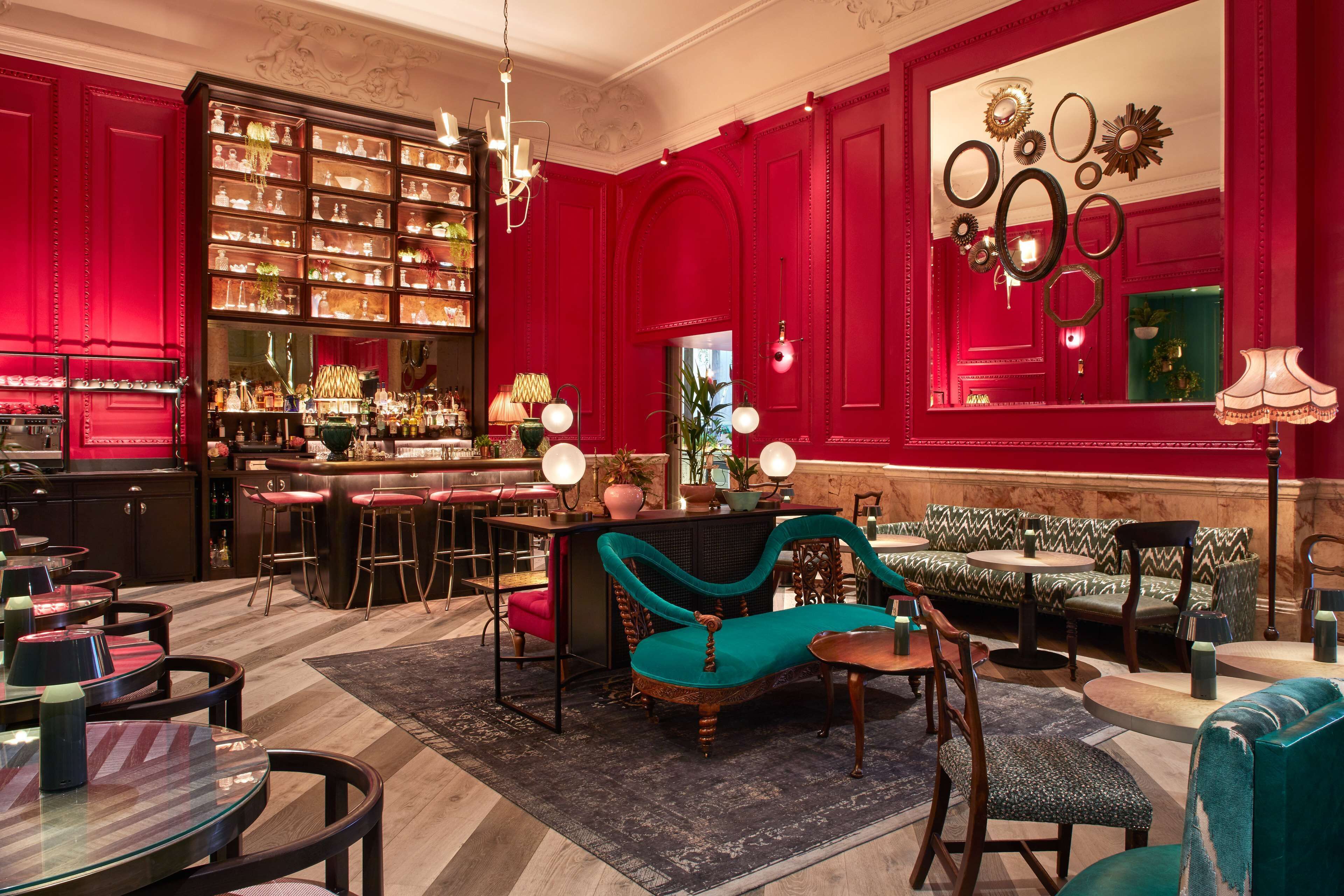 A red-walled room with a bar, seating area, and a large bookcase.