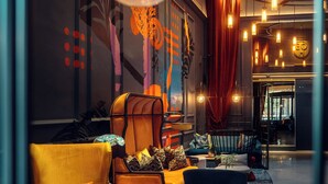 A modern interior with a curved ceiling, a seating area with a yellow sofa and a blue armchair, and a large window with curtains. - ANDAZ LONDON LIVERPOOL STREET, BY HYATT (London)
